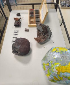 Table présentant plusieurs échantillons de roches et de matériaux géologiques, accompagnés de lames d’observation et d’un globe terrestre.