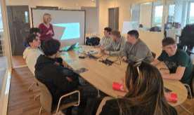 Dans une salle de réunion, une intervenante présente une formation à des élèves assis autour d'une table.