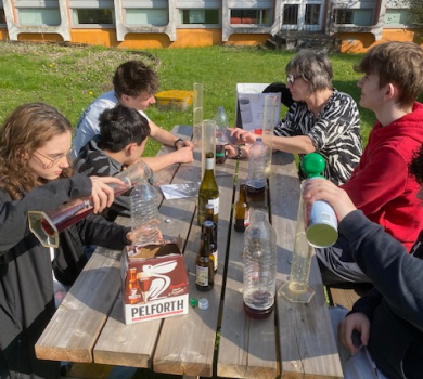 Des élèves assis à une table en train de créer des pièges à frelons en mélangeant différents liquides dans des bouteilles.