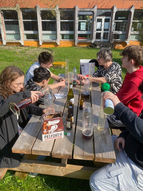 Des élèves assis à une table en train de créer des pièges à frelons en mélangeant différents liquides dans des bouteilles.