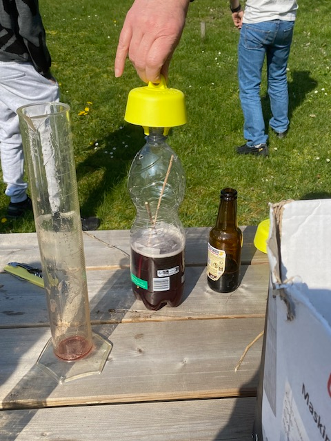 Une bouteille avec un liquide dedans, on est en train de mettre un bouchon ave un crochet pour pouvoir le suspendre.