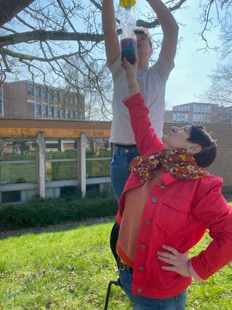 Un élève et une professeure sont en train d'accrocher un piège à frelon dans un arbre.