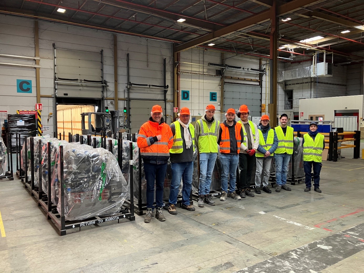 Élèves en CAP Conducteur Routier et professionnels posant dans un entrepôt industriel aux côtés de moteurs conditionnés prêts à être transportés.