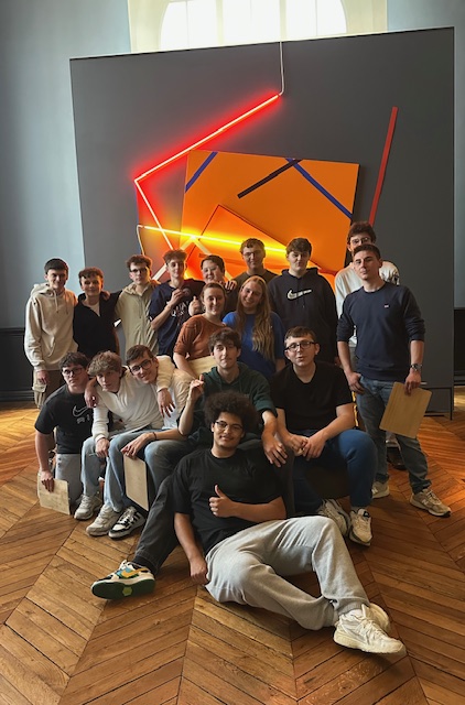 Un groupe d'élève devant une œuvre faites avec des néons.