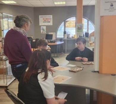 Groupe d’élèves échangeant avec une intervenante autour d’une table, analysant des documents dans le cadre d’un atelier journalistique à Canopé Amiens