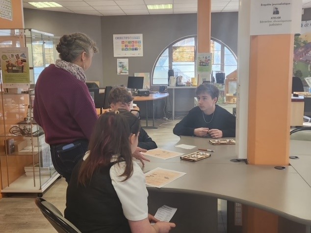 Groupe d’élèves échangeant avec une intervenante autour d’une table, analysant des documents dans le cadre d’un atelier journalistique à Canopé Amiens