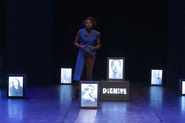 Comédienne seule sur scène entourée de portraits lumineux lors du spectacle « J’ai plusieurs terres », évoquant mémoire, identité et héritage