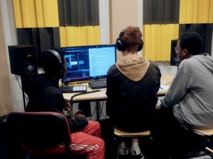 Trois élèves équipés de casques audio travaillent ensemble sur un logiciel de création numérique et sonore dans un studio.