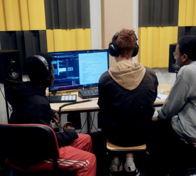 Trois élèves équipés de casques audio travaillent ensemble sur un logiciel de création numérique et sonore dans un studio.